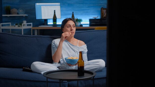 Geconcentreerde vrouw die popcorn eet en een interessante film op tv kijkt, alleen thuis...