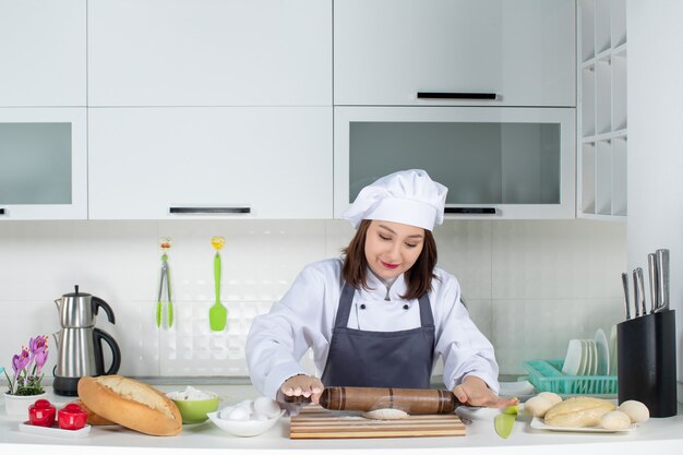 Geconcentreerde vrouwelijke commischef in uniform die achter tafel staat en gebak bereidt in de witte keuken