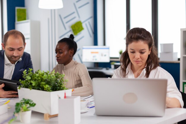 Geconcentreerde vrouwelijke manager die op laptop typt, op internet surft terwijl hij aan een bureau zit geconcentreerd met multitasking