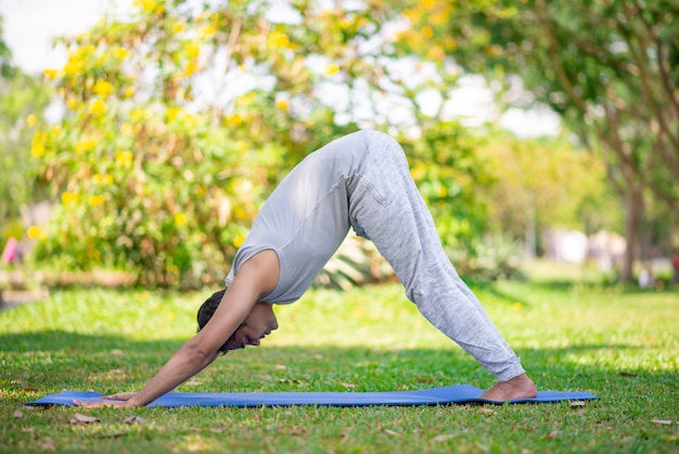 Geconcentreerde yogi die op parkgras uitoefent. Jonge Indiase man met yoga naar beneden gericht