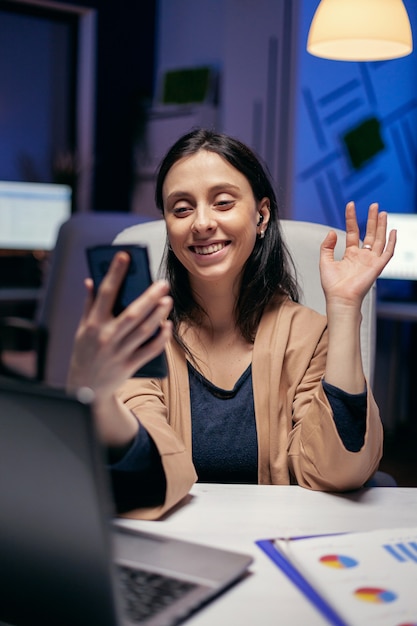 Gedag zeggen tijdens een teleconferentie met ondernemers die overuren maken. Vrouw die aan financiën werkt tijdens een videoconferentie met collega's 's nachts op kantoor.