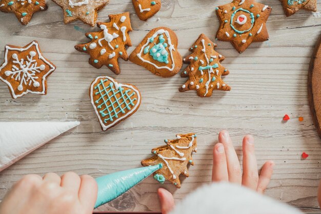 Gedeeltelijk wazige handen van jongen versieren peperkoekkoekjes met blauw glazuur in de keuken. kind maakt koekjes