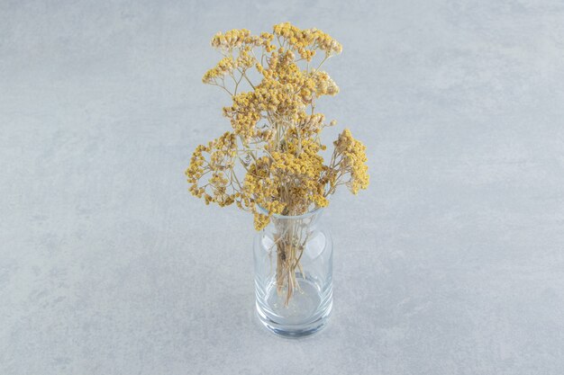 Gedroogde gele bloemen in glazen pot.