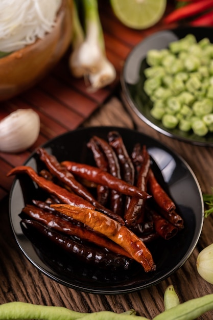 Gedroogde pepers gebakken in een zwarte plaat met linzen. Komkommers en knoflook worden op de houten tafel geplaatst