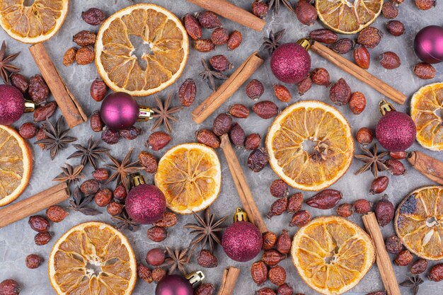 Gedroogde sinaasappel met kerstballen en rozenbottels op stenen oppervlak.