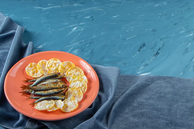 Gedroogde sprot en kaas chips in een bord op de handdoek, op de blauwe achtergrond.