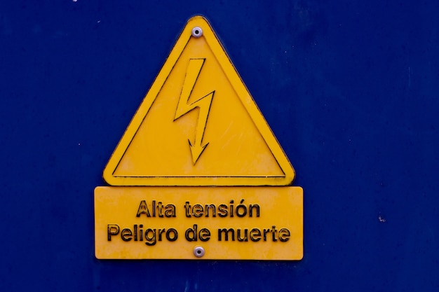 Geel beeld van een hoogspanningsbord op een blauwe achtergrond met het bord in het spaans