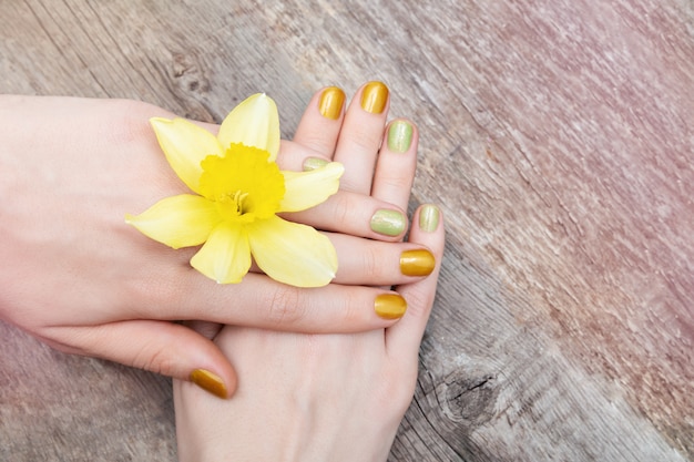 Geel nagelontwerp. Vrouwelijke hand met glitter manicure met narcissus bloemen.