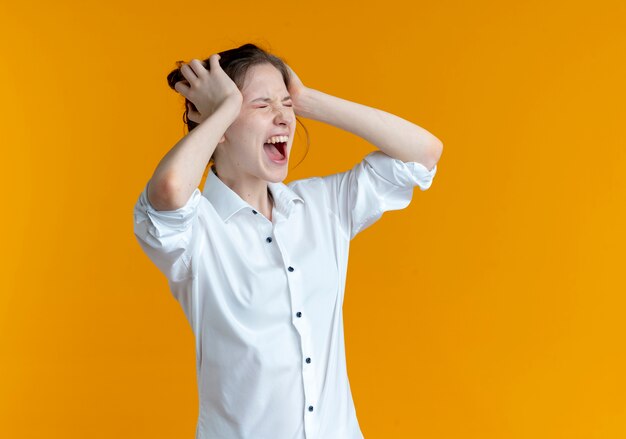 Geërgerd blond Russisch meisje houdt hoofd met twee handen geïsoleerd op oranje ruimte met kopie ruimte