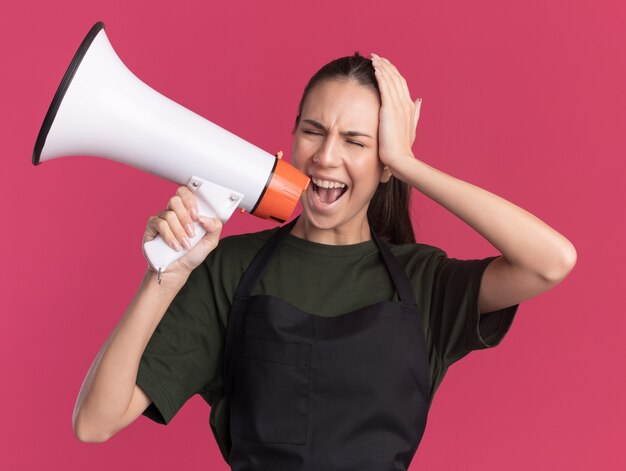 Geërgerd jong brunette kappersmeisje in uniform legt hand op hoofd en schreeuwt in luidspreker