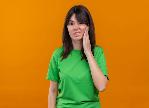 Geërgerd jong Kaukasisch meisje in groen shirt houdt gezicht en kijkt naar camera op geïsoleerde oranje achtergrond