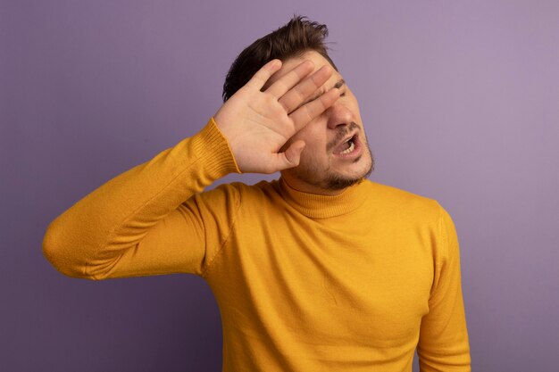 Geërgerd jonge blonde knappe man geïsoleerd op paarse muur