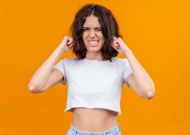 Geërgerd jonge mooie vrouw handen op oren zetten geïsoleerde oranje muur