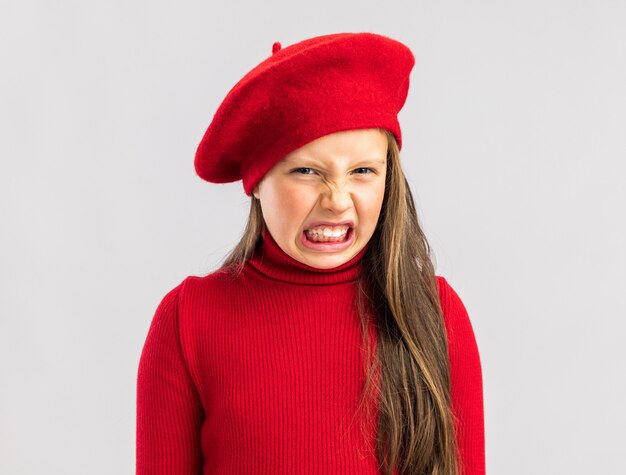 Geërgerd klein blond meisje met rode baret geïsoleerd op een witte muur met kopieerruimte