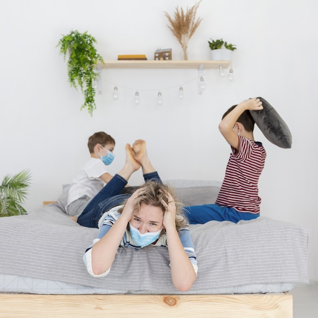 Gratis foto geërgerd moeder met medisch masker en kinderen vechten met kussens