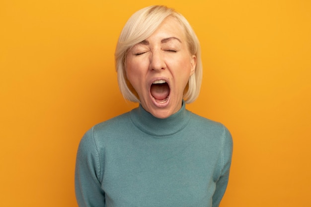 Geërgerd mooie blonde Slavische vrouw staat met gesloten ogen schreeuwen tegen iemand geïsoleerd op oranje muur