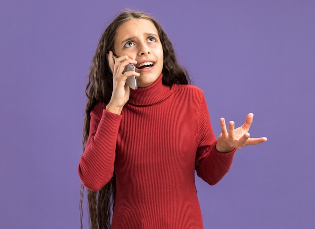 Geërgerd tienermeisje praten over telefoon opzoeken met lege hand geïsoleerd op paarse muur