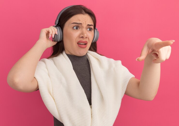 Gratis Foto geërgerde jonge mooie vrouw die een koptelefoon draagt en grijpt, kijkend en wijzend naar de zijkant geïsoleerd op roze muur