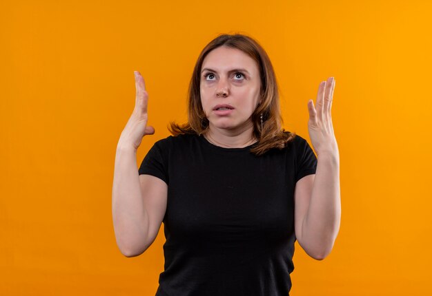 Geërgerde jonge toevallige vrouw die handen opheft die omhoog op geïsoleerde oranje ruimte met exemplaarruimte kijken