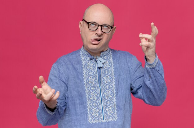 Geërgerde volwassen Slavische man in blauw shirt met optische bril die handen open houdt en omhoog kijkt