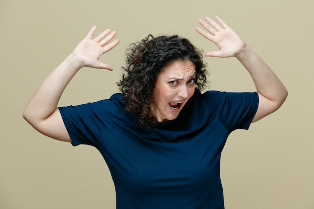 geërgerde vrouw van middelbare leeftijd die een t-shirt draagt en naar de camera kijkt en de handen omhoog steekt schreeuwend geïsoleerd op een olijfgroene achtergrond