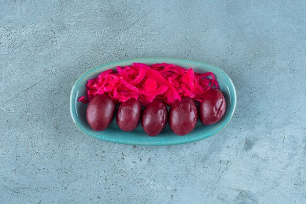 Gefermenteerde rode zuurkool met pruimen op een bord, op de blauwe tafel.