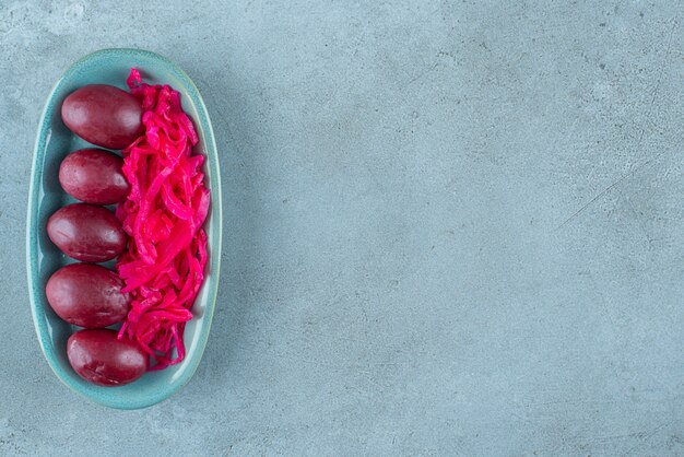 Gefermenteerde rode zuurkool met pruimen op een bord, op de blauwe tafel.