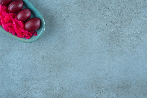 Gefermenteerde rode zuurkool met pruimen op een bord, op de blauwe tafel. Gratis Foto