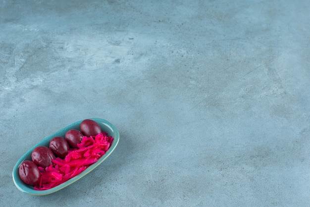 Gefermenteerde rode zuurkool met pruimen op een bord, op de blauwe tafel.