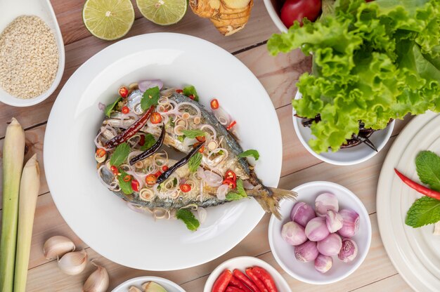 Gefrituurde makreel gegarneerd met laos, peper, munt, rode ui in een witte schotel.