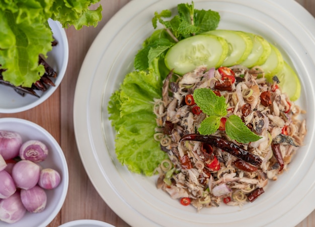 Gefrituurde makreel gegarneerd met laos, peper, munt, rode ui in een witte schotel.