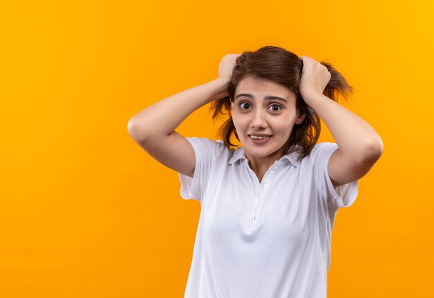 Gefrustreerd jong meisje met kort haar, gekleed in een wit poloshirt dat aan haar haar trekt