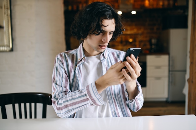 Gefrustreerde jongeman slecht nieuws lezen tijdens het surfen op internet op mobiel. Bezorgde student kan niet bellen omdat hij zijn saldo moet opladen.