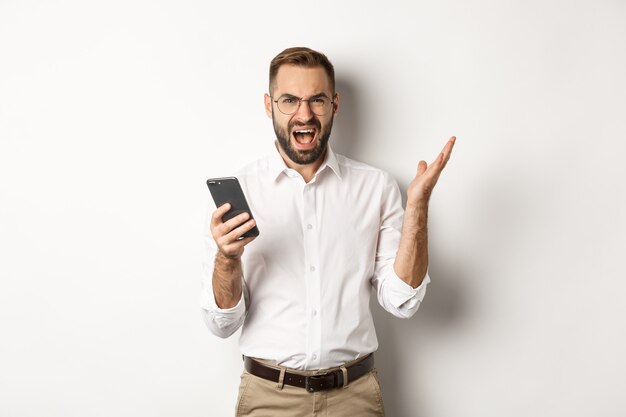 Gefrustreerde man die mobiele telefoon gebruikt en teleurgesteld, klagend, staande kijkt.