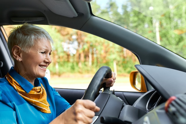 Gefrustreerde rijpe vrouw grimassen, met een ongelukkige blik, zittend in de auto bij de bestuurder, gestrest omdat ze midden op de weg geen benzine meer had.