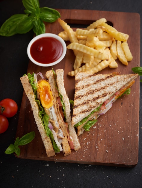Gratis foto gegrild en sandwich met spek, gebakken ei, tomaat en sla geserveerd op een houten snijplank