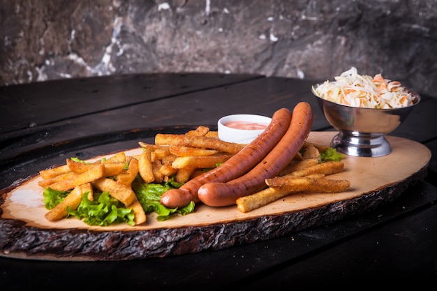 Gegrilde hotdogs, frietjes, ketchup en salade op een snijplank