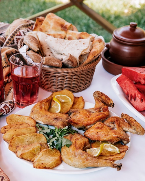 Gegrilde kip met aardappelschijfjes geserveerd met citroen, kruiden, glas rode drank en brood.