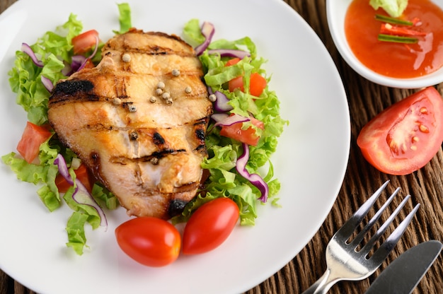 Gegrilde kip op een witte plaat met een salade van tomaten, wortelen en pepers in stukjes gesneden.