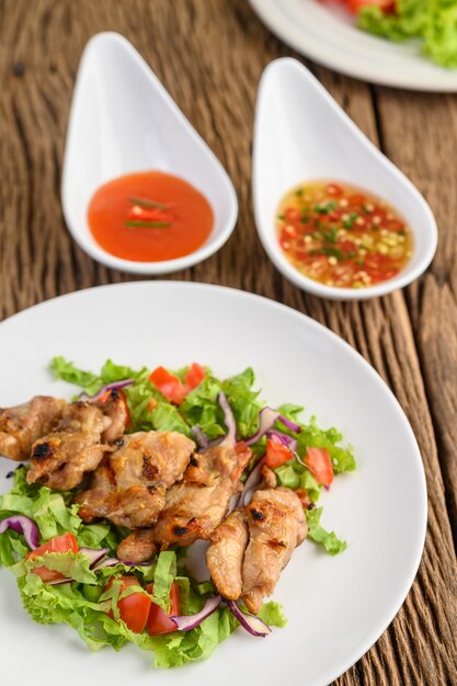 Gegrilde kip op een witte plaat met een salade van tomaten, wortelen en pepers in stukjes gesneden.