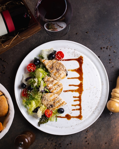 Gegrilde kippenborst geserveerd met groentesalade, olijven en glas wijn