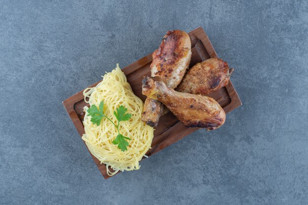 Gegrilde kippenpoten en spaghetti op een houten bord.