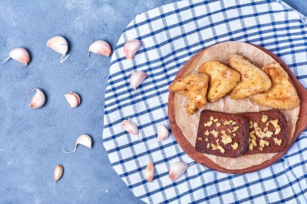 Gegrilde kippenvleugels met kruiden en sneetjes brood op een houten bord op blauw