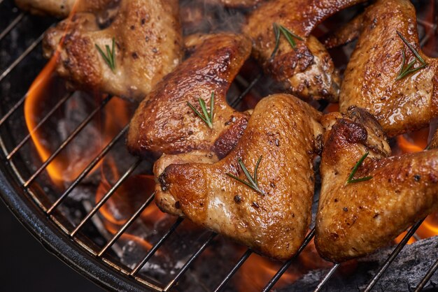 Gegrilde kippenvleugels op de vlammende grill met gegrilde groenten in barbecuesaus met peperzaad, rozemarijn, zout.