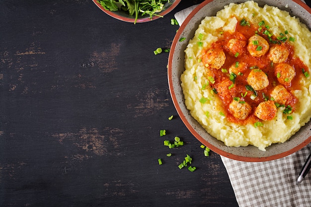 Gehaktballetjes in tomatensaus met aardappelpuree in kom.