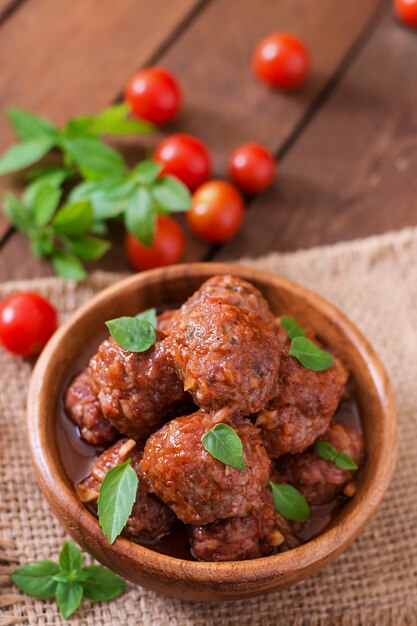 Gehaktballetjes in zoetzure tomatensaus en basilicum in een houten kom