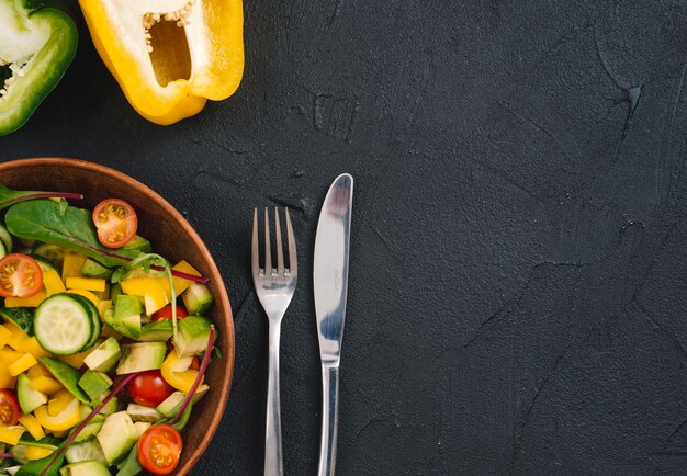 Gehalveerde paprika en gemengde groentesalade met bestek op zwarte concrete achtergrond