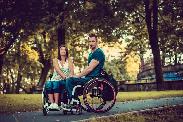 Gehandicapt jong koppel op twee rolstoelen zoenen in herfst park.