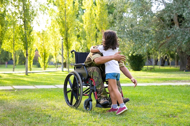 Gehandicapte gepensioneerde militaire man vergadering en dochtertje knuffelen in park. Veteraan van oorlog of naar huis terugkeren concept