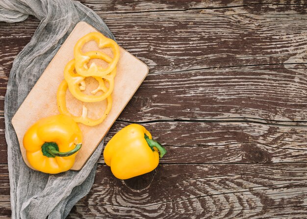 Geheel en plakjes gele paprika op snijplank over de grijze textiel tegen houten bureau